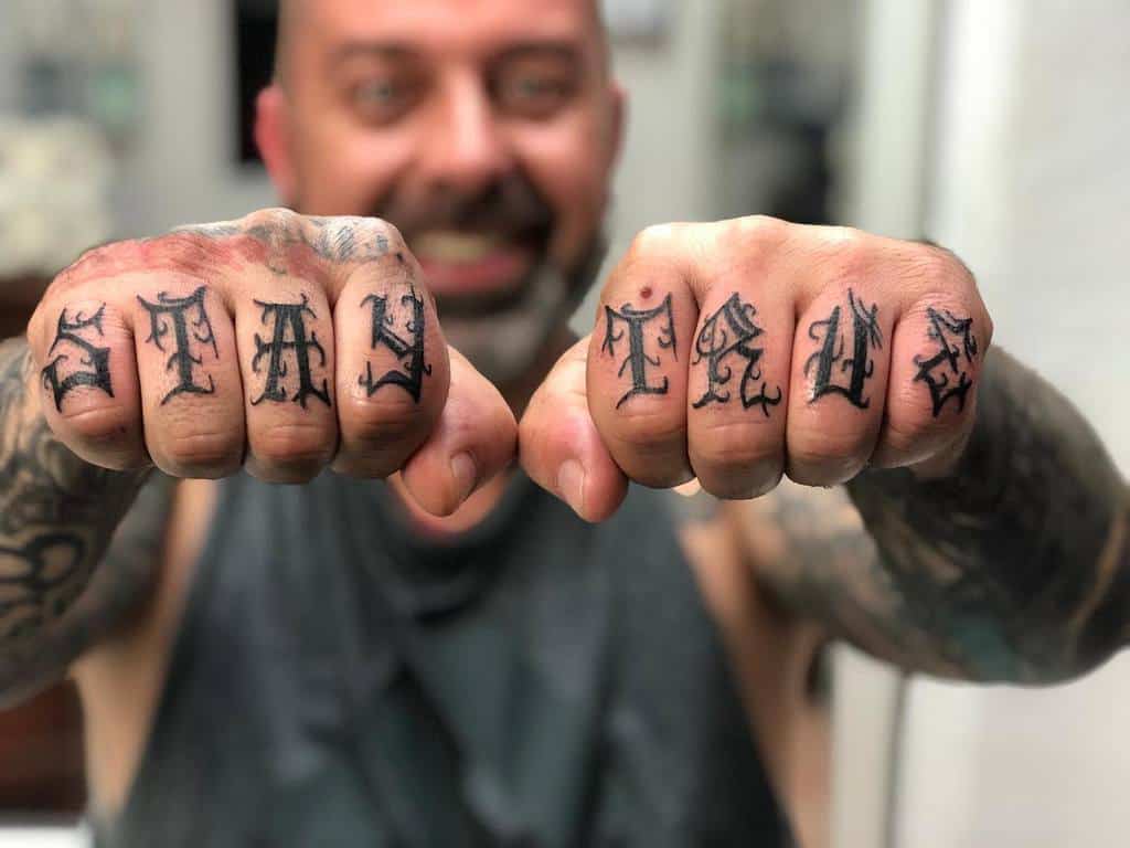 Man showing knuckle tattoos that say "Stay True"