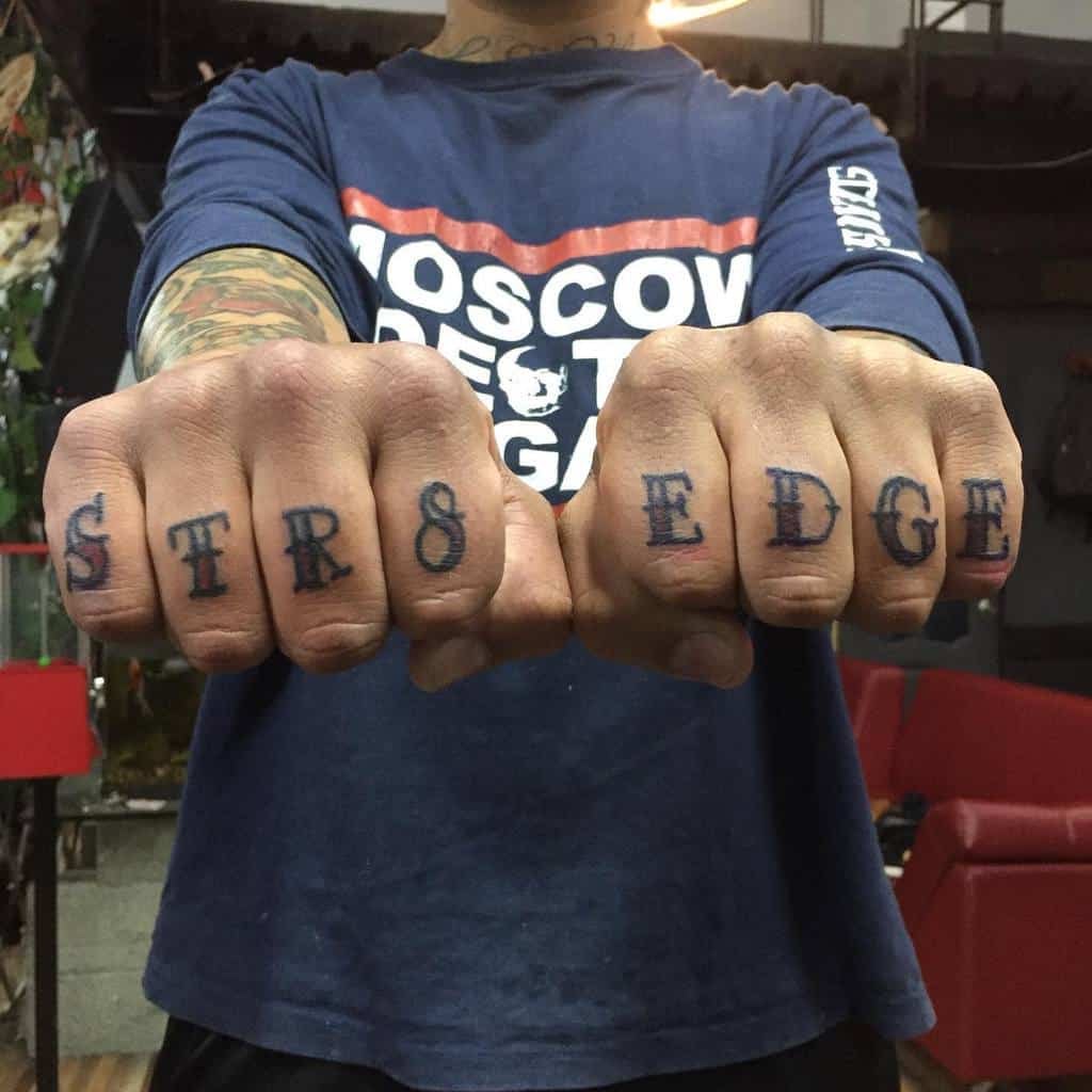 Close-up of hands with "STR8 EDGE" tattooed on the fingers