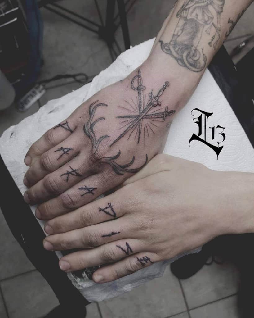 Detailed hand tattoo featuring crossed swords and radiant lines, with minimalist letter tattoos on the fingers for a bold look