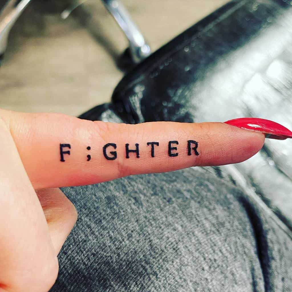 Finger with the word "F;GHTER" tattooed on it