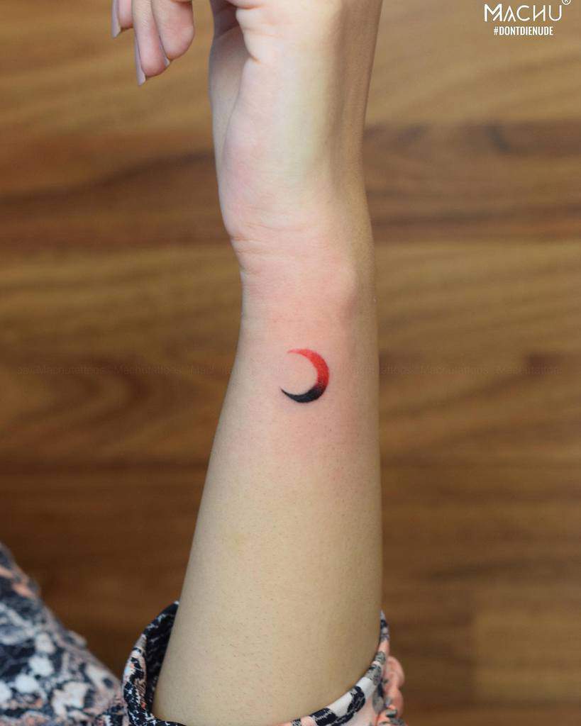 A forearm tattoo of a red and black crescent moon on light skin