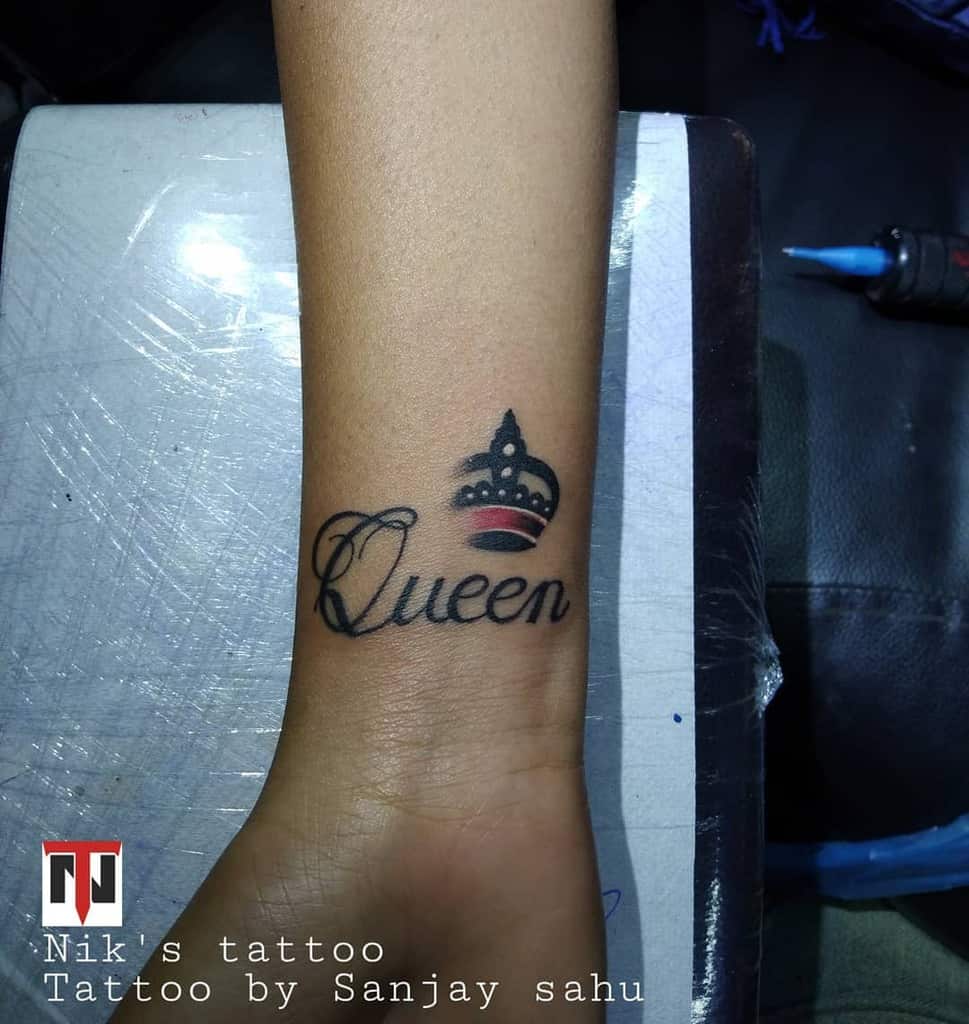 Tattoo of the word "Queen" with a crown on a wrist