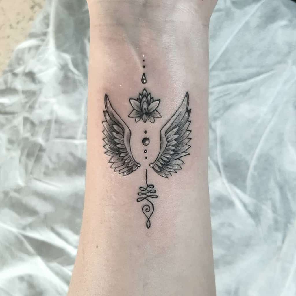 Tattoo of wings, a lotus flower, and decorative elements on a wrist