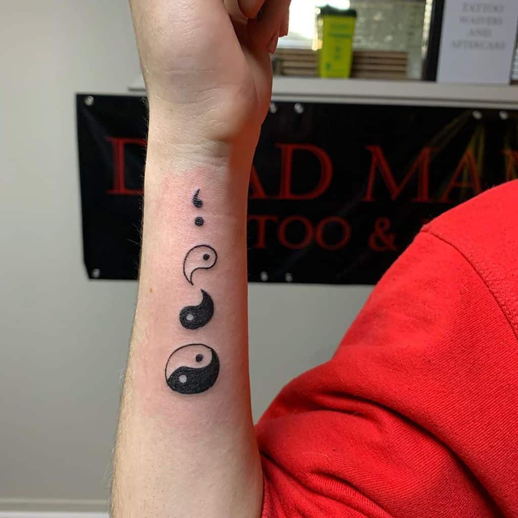 Wrist tattoo of a black and white yin-yang symbol with smaller versions above it