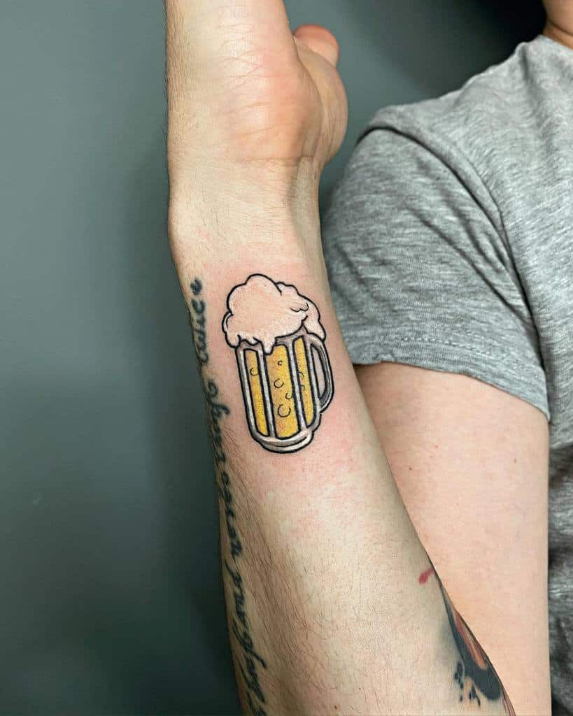 Forearm tattoo of a frothy beer mug with cursive script above it