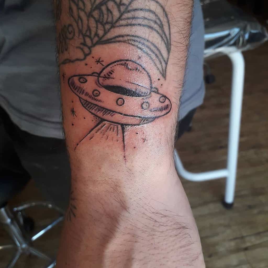 Wrist with a tattoo of a UFO beaming light, surrounded by stars and other designs