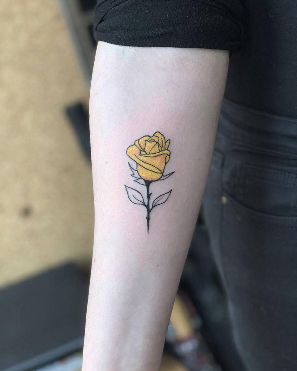 Forearm tattoo of a single yellow rose with green leaves drawn in a minimalist style