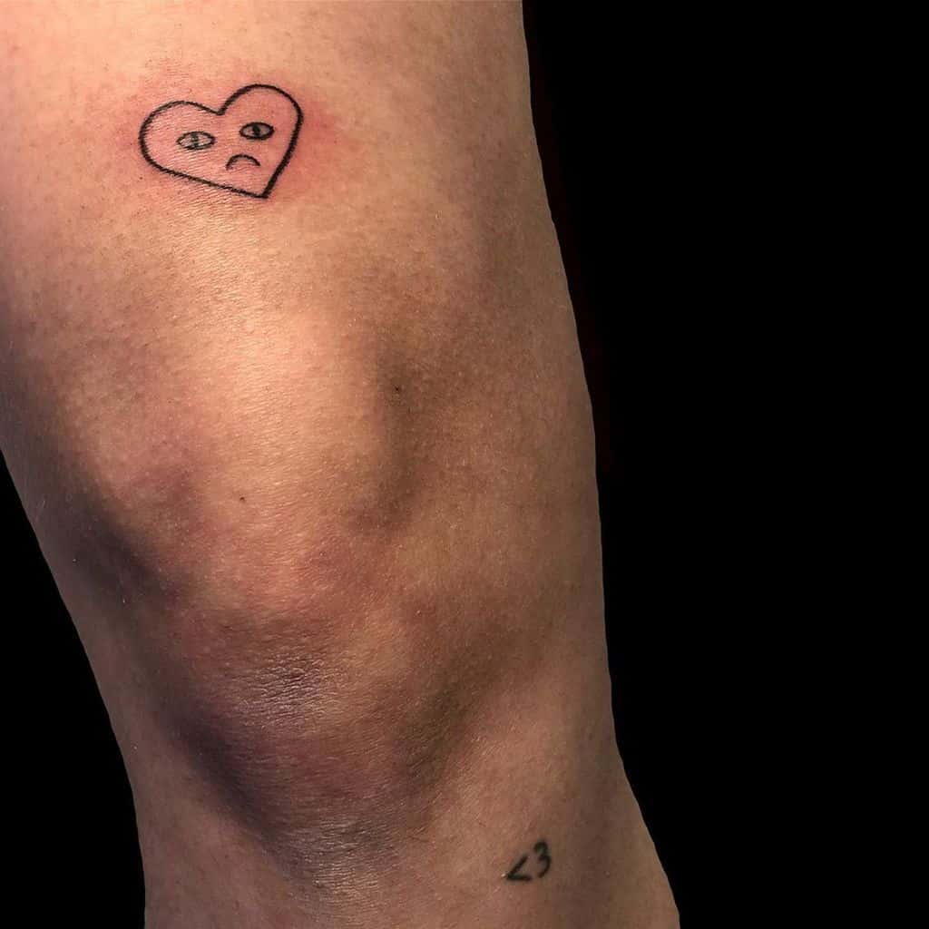 Minimalist tattoo of a small heart with sad facial features