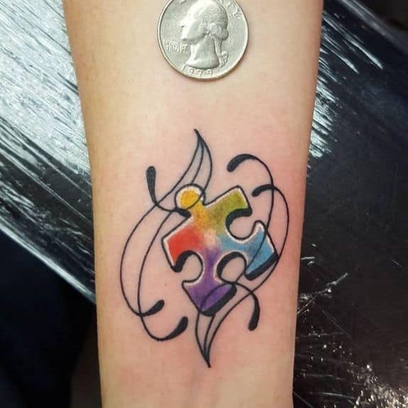 Small full color wrist tattoo of a multi-colored puzzle piece with decorative, line work flourishes.