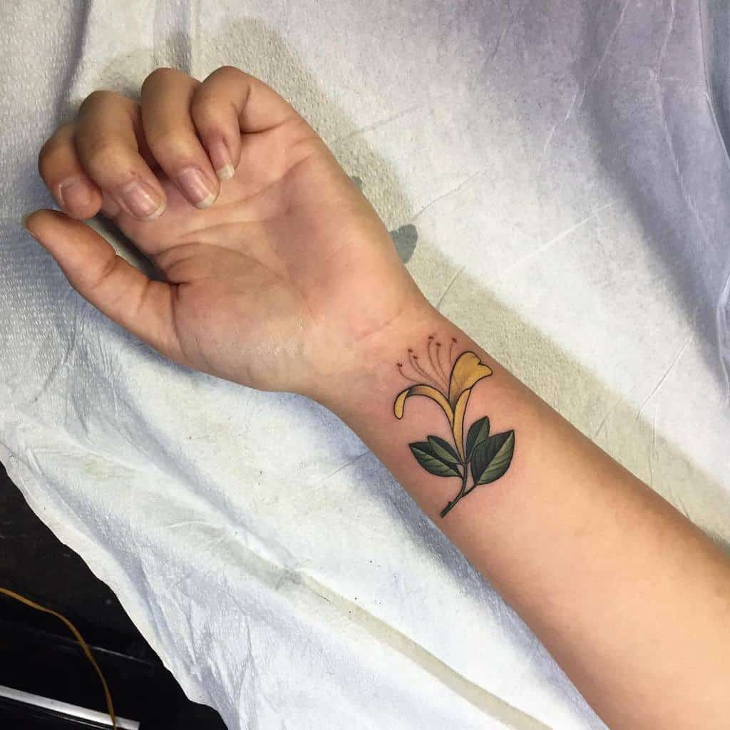 A yellow honeysuckle flower tattoo on a wrist with vibrant green leaves