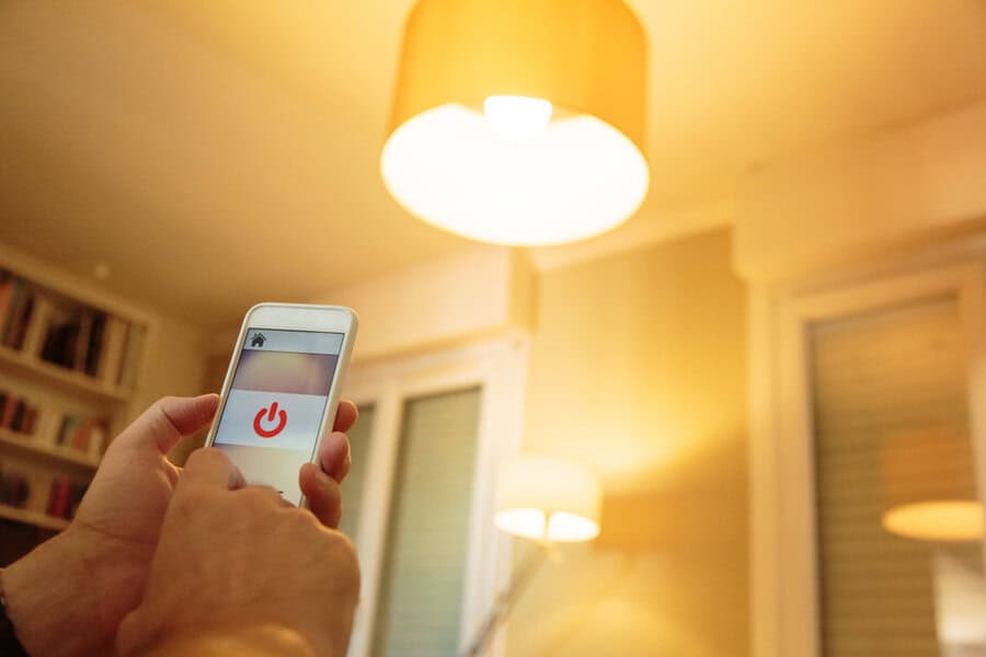 Person using a smartphone app to remotely turn on a ceiling light in a cozy, well-lit room