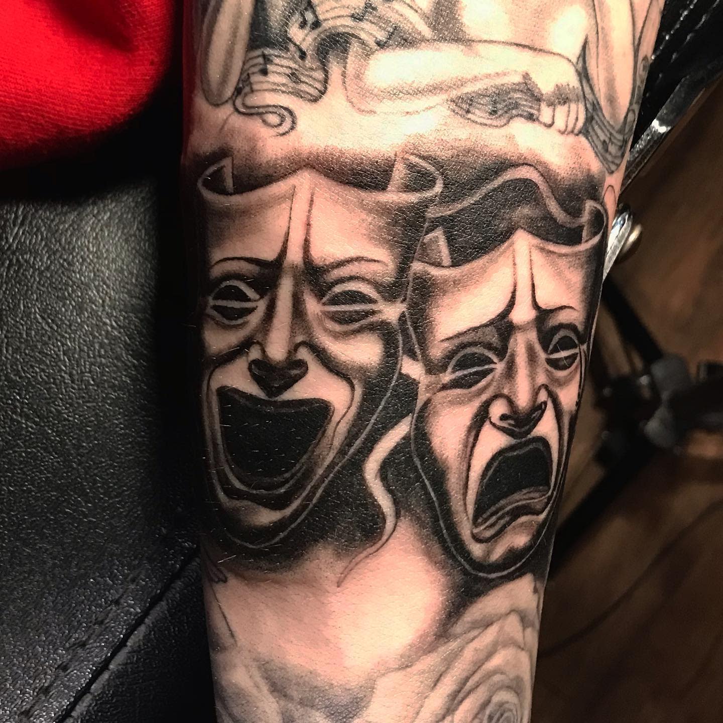 Tattoo of dramatic theater masks, one smiling, one frowning, in black and grey shading