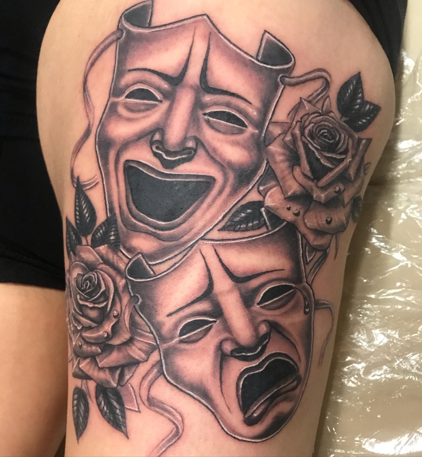 Tattoo of Comedy and Tragedy masks with roses on a thigh