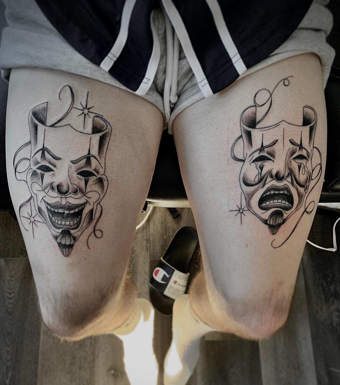 A pair of thigh tattoos depicting comedy and tragedy theatre masks on a seated individual
