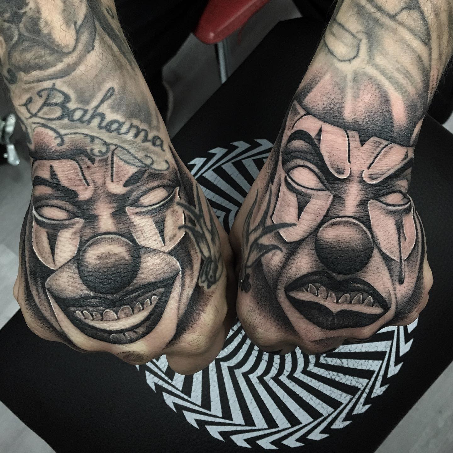 Two hands display black and white tattoos of sinister clowns on the knuckles and backs