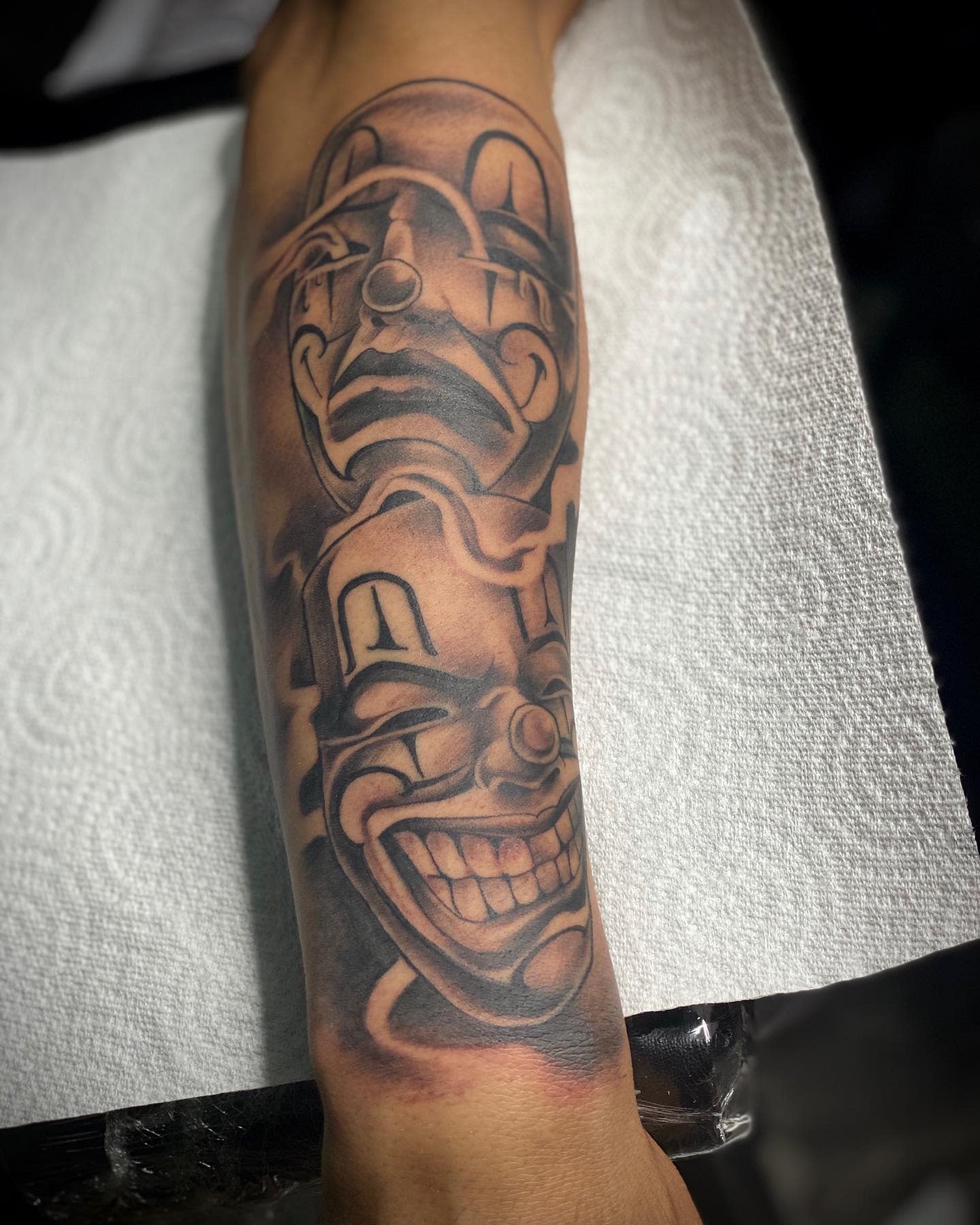 A forearm tattoo displays two masks, one happy and one sad