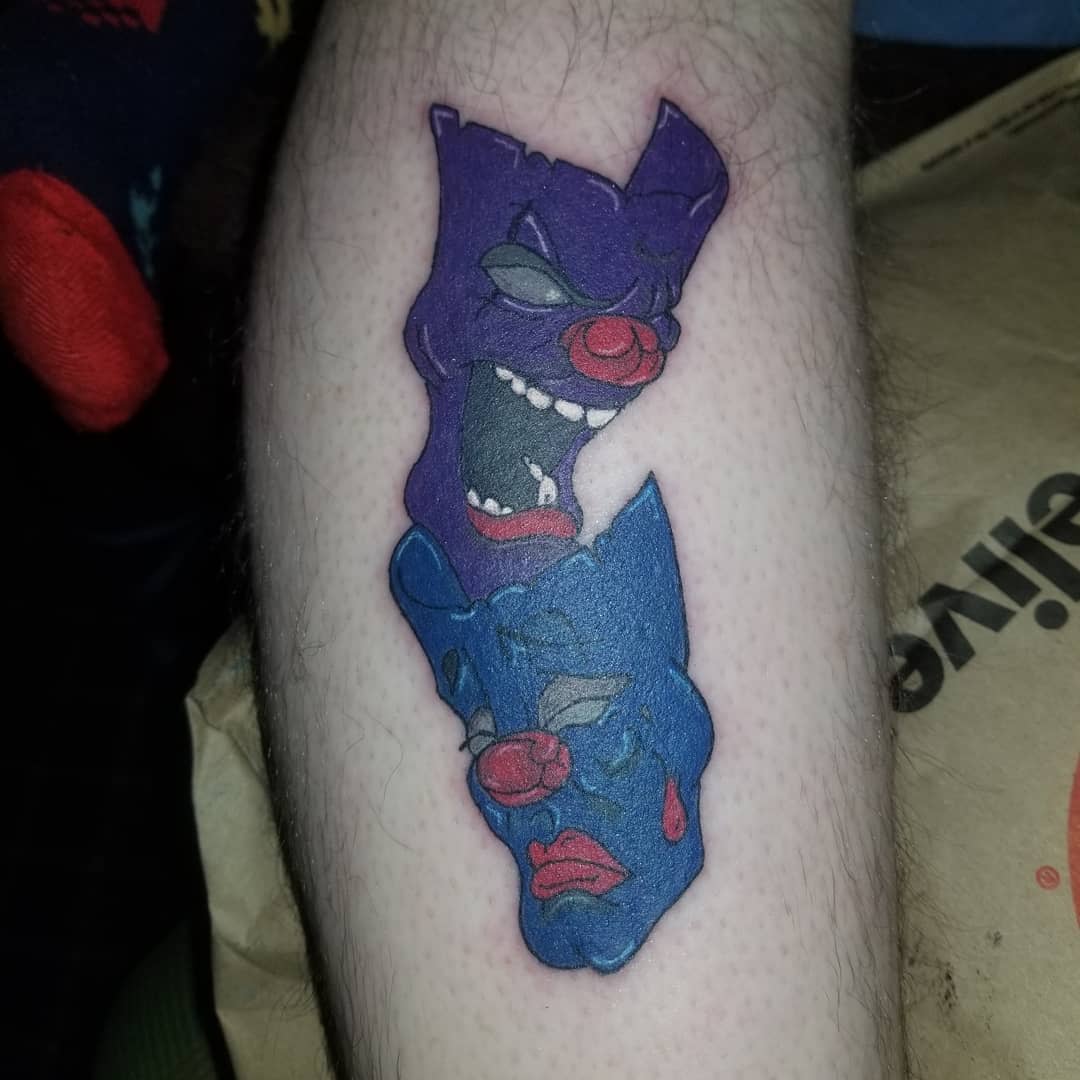 Tattoo on leg of two abstract mask faces, one purple and angry, one blue and sad, interconnected
