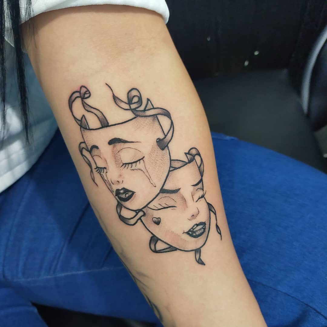 A tattoo of two theatre masks on an arm, one sad with a tear and the other happy on a forearm
