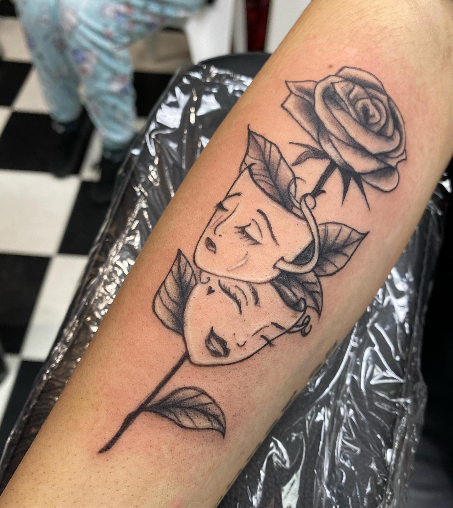 Tattoo of two drama masks and a rose on an arm