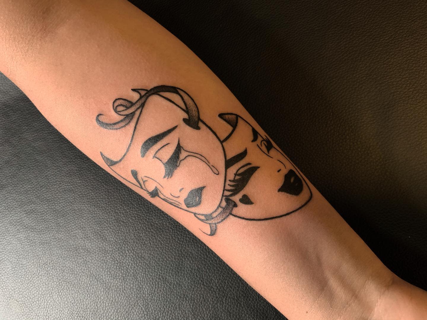 Tattoo of a crying woman mask with a happy mask overlay on an arm