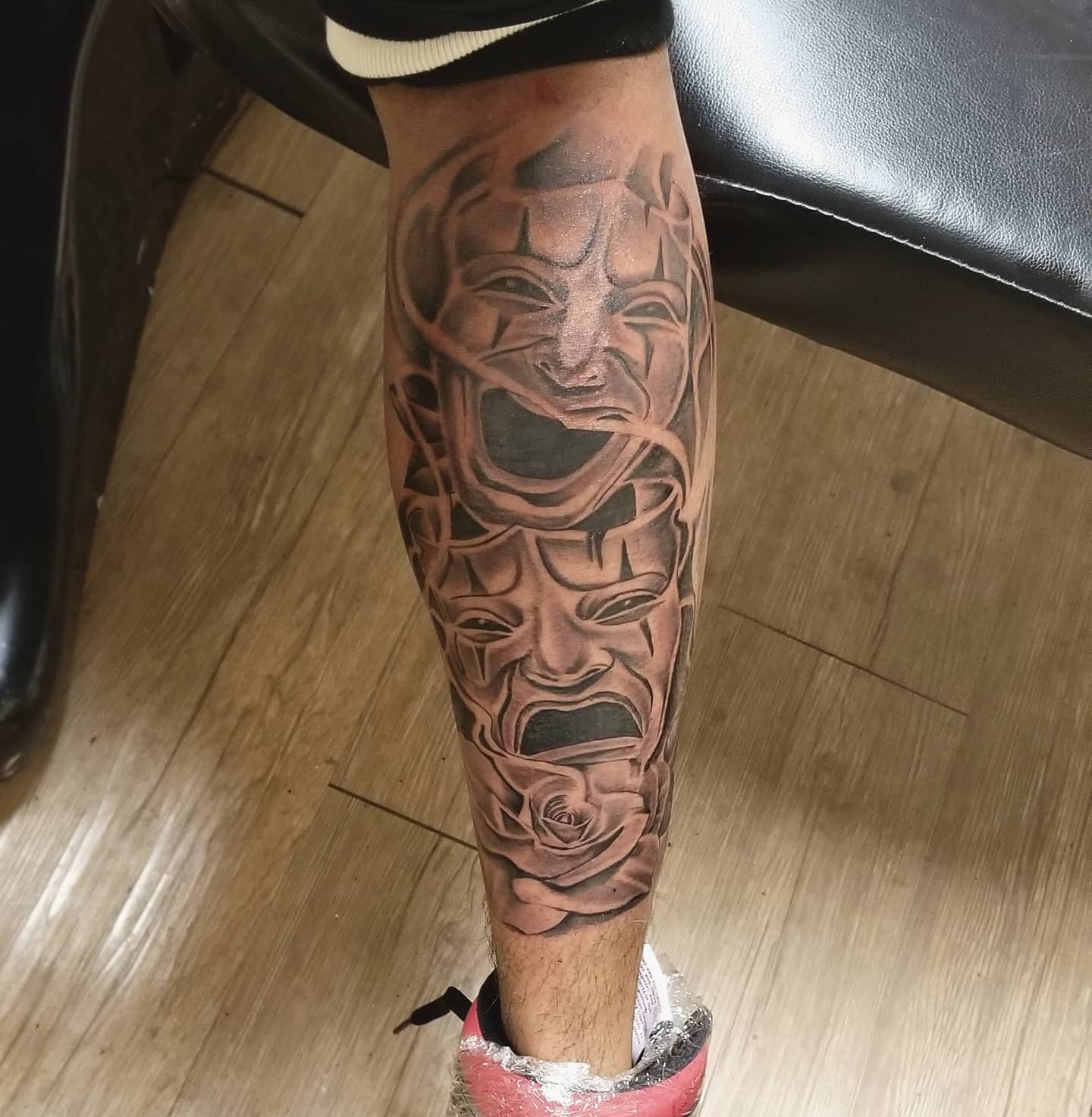 A leg tattoo featuring three theatrical masks and a rose
