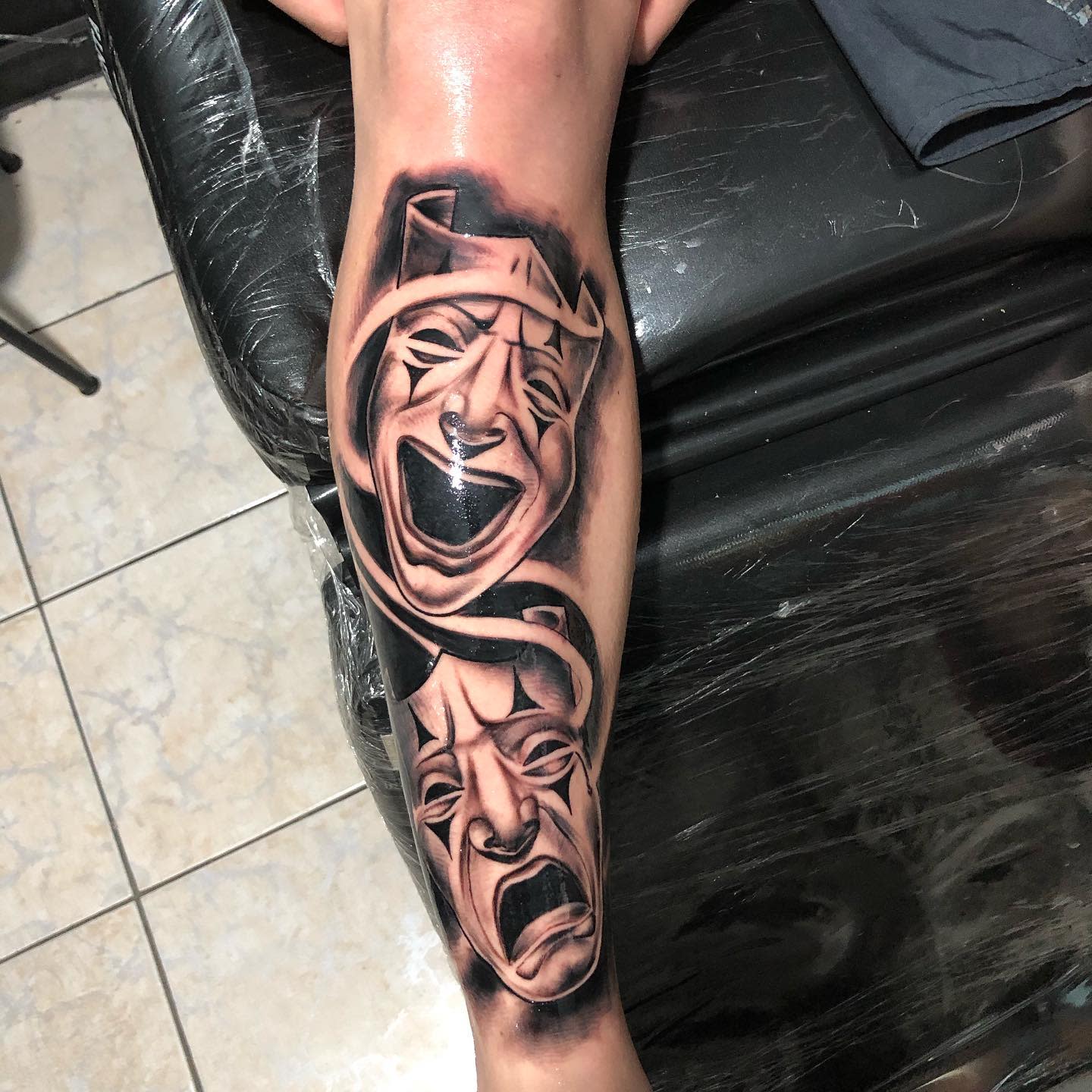 Tattoo on leg of theatrical masks, one laughing and the other crying