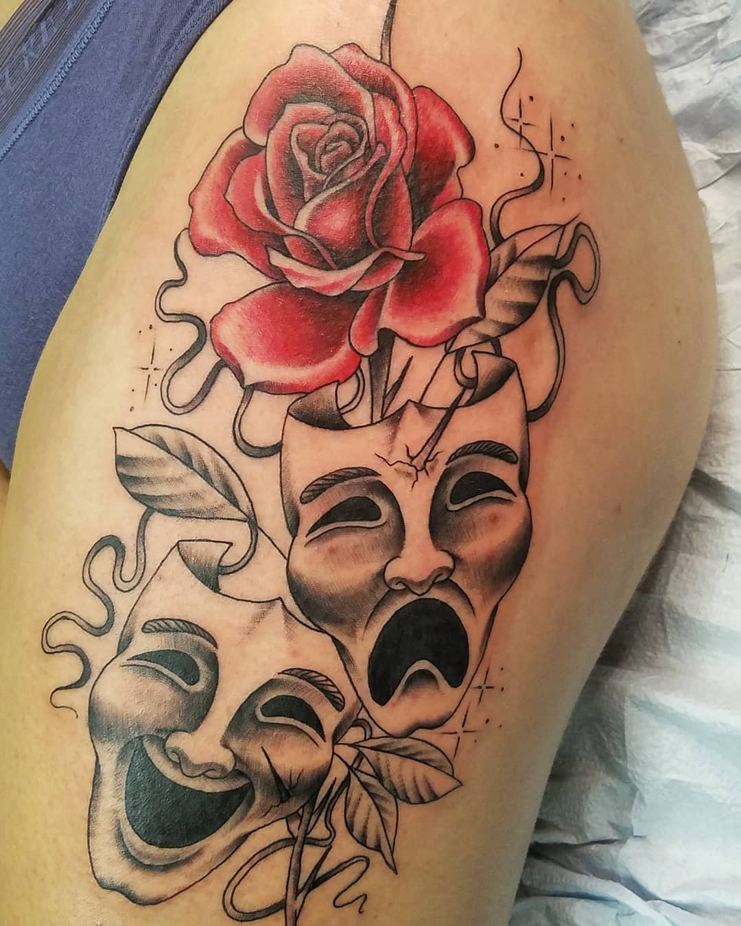 Tattoo of a rose with theater masks one smiling and one crying intertwined with vines