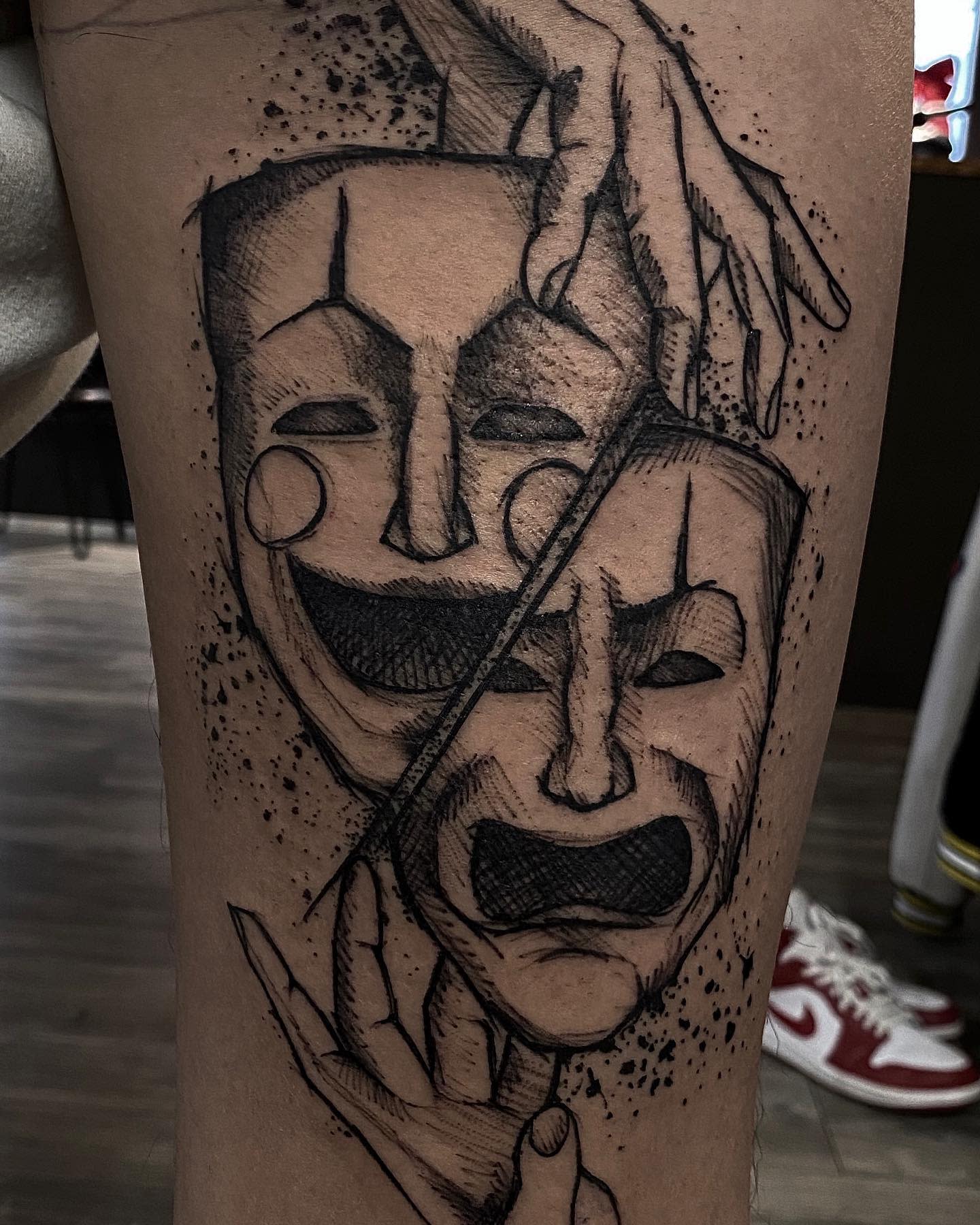 Tattoo of comedy and tragedy masks on a leg surrounded by hands and dotted shading