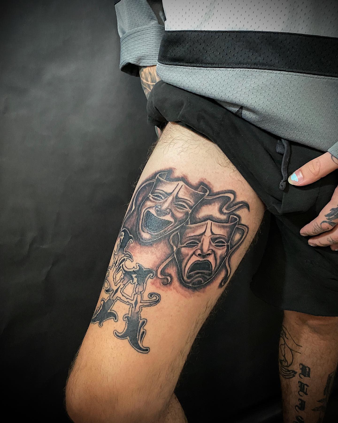 A leg tattoo featuring comedy and tragedy masks intertwined with a decorative design