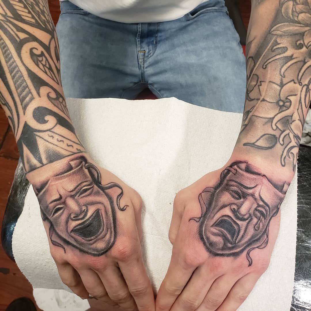 Two hands with tattoos of comedy and tragedy masks on the outer sides