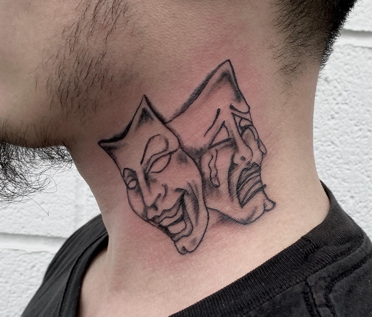 Close-up of neck tattoo depicting comedy and tragedy masks in black ink