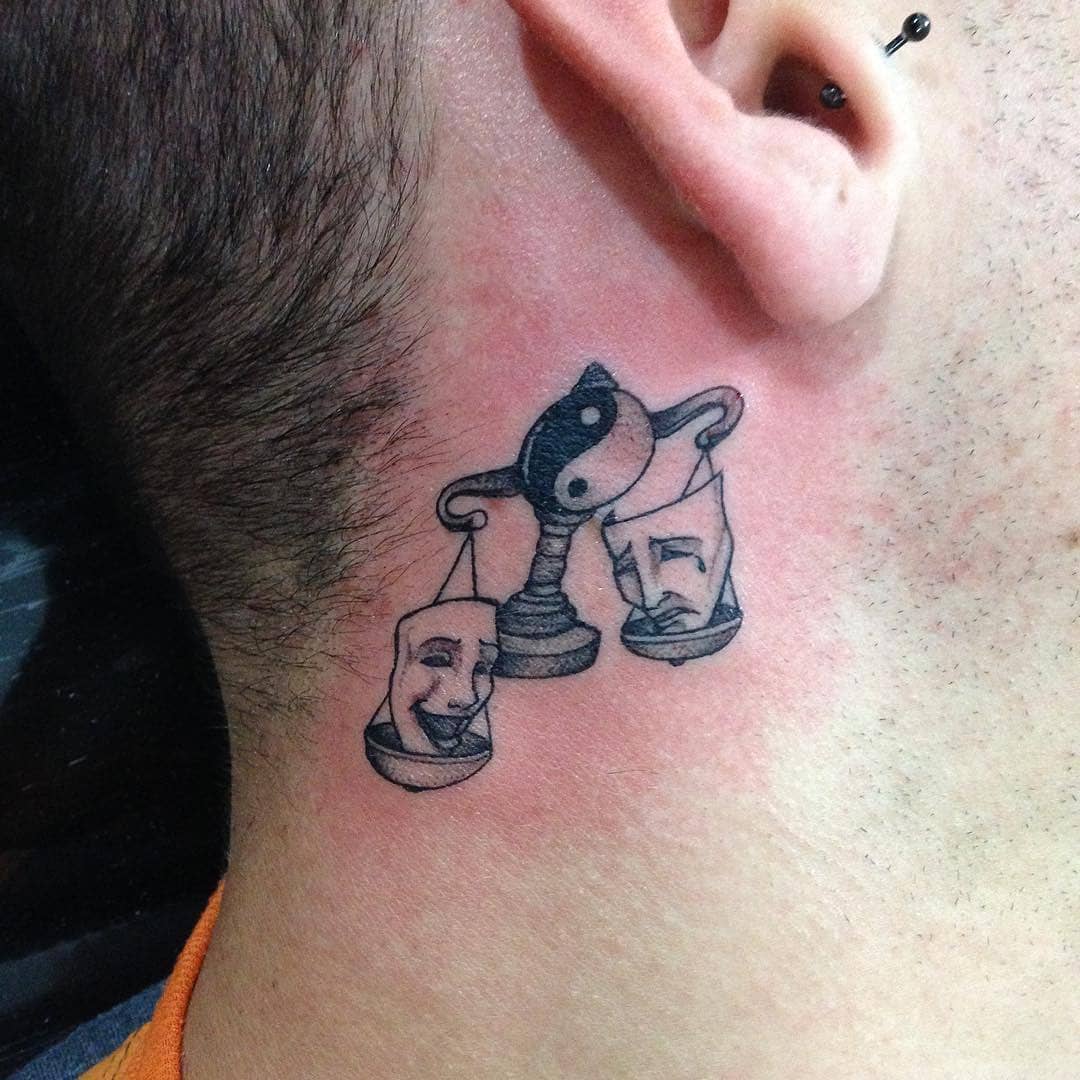 Tattoo behind ear: scales balancing comedy and tragedy masks with yin-yang symbol as fulcrum