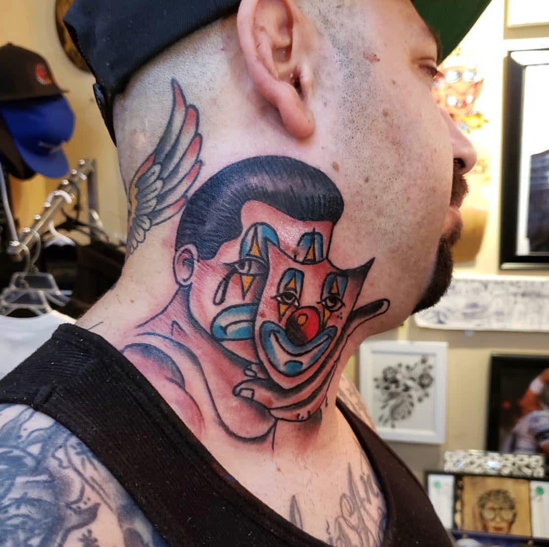 Man with a neck tattoo of a sad clown face holding happy face mask