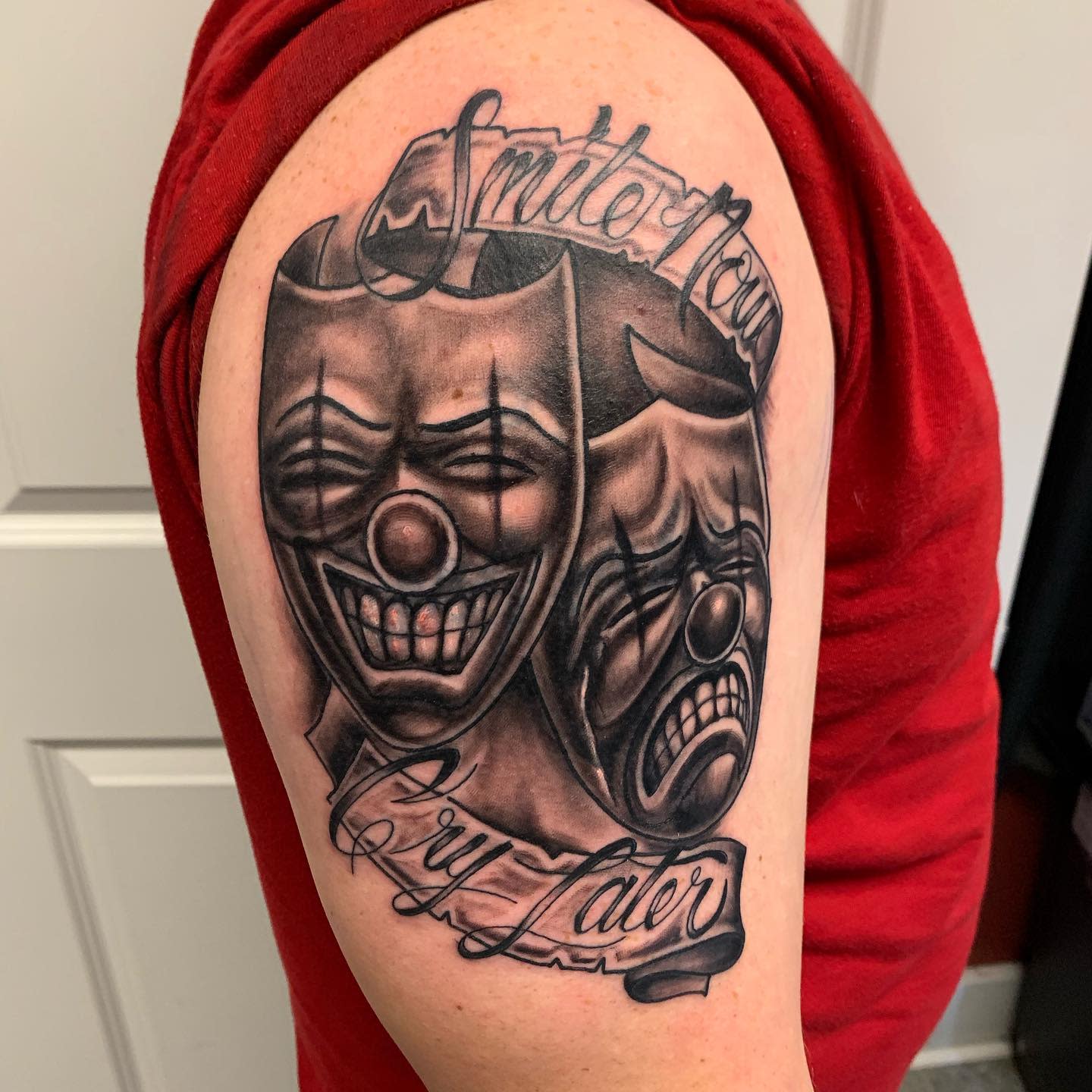 Tattoo of comedy and tragedy masks with text "Smile Now Cry Later" on upper arm