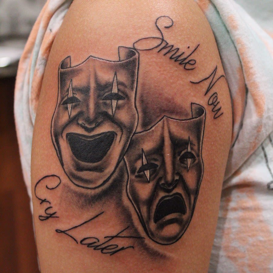 Tattoo of "Smile Now Cry Later" with comedy and tragedy masks on an upper arm
