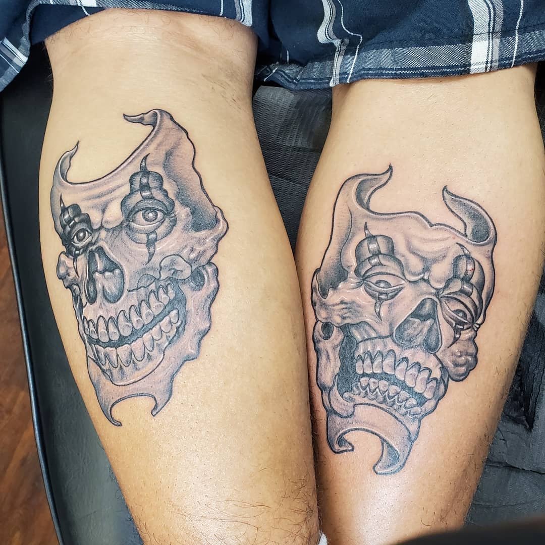 Two thighs with black and grey skull tattoos featuring horns and grinning expressions