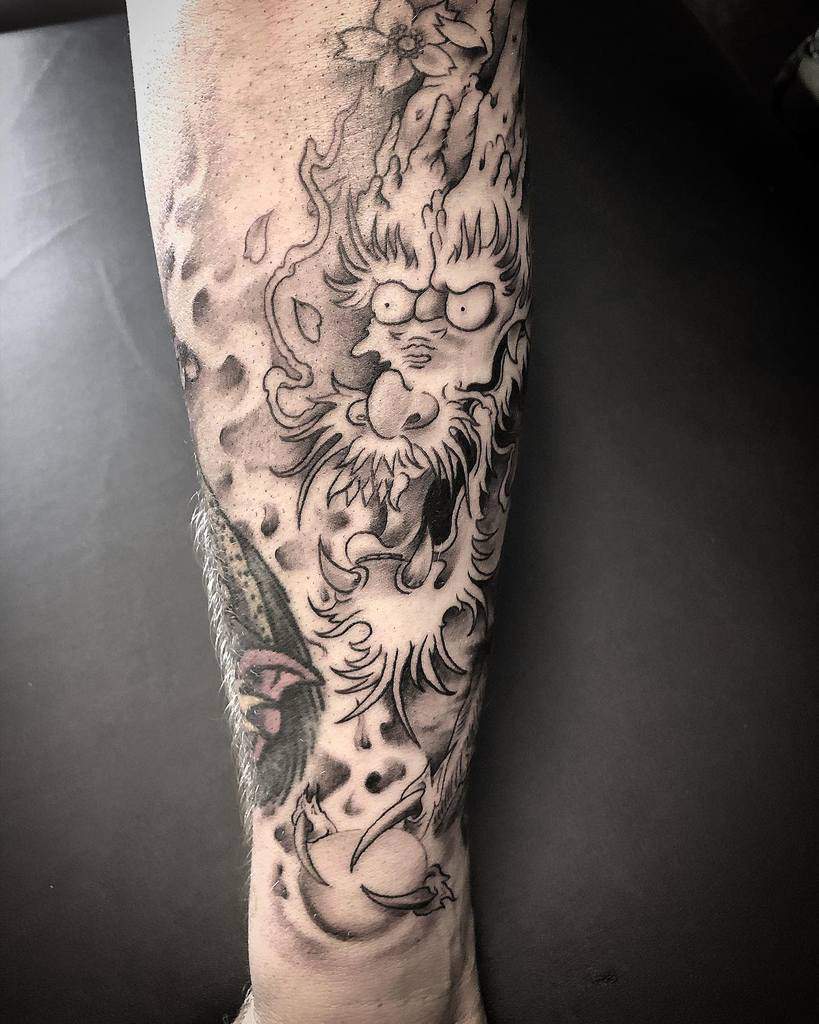 Tattoo of a fiery dragon in traditional Japanese style, detailed with flames and shading, inked on the lower arm