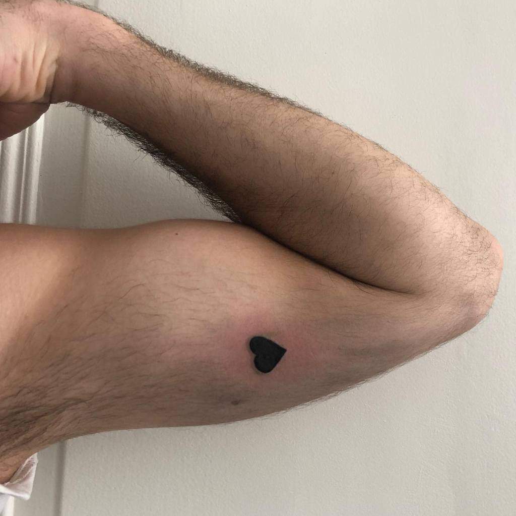 Solid black heart tattoo on the inner bicep, positioned near the crease of the arm