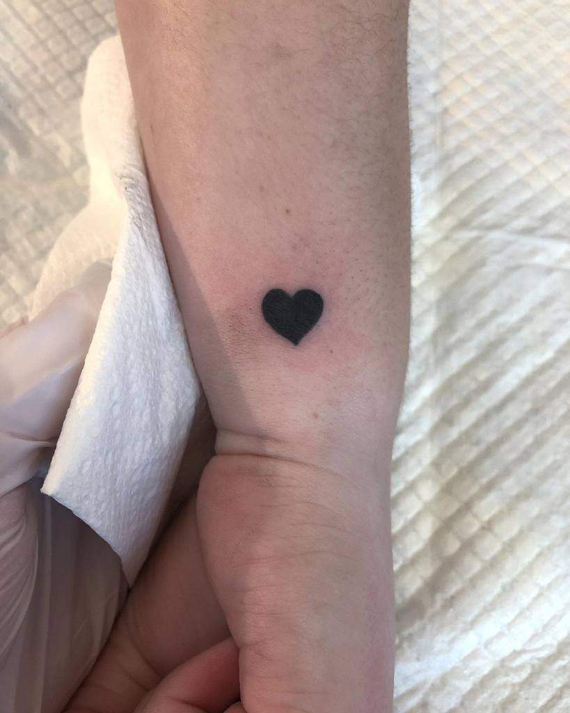 A minimalist solid black heart tattoo that symbolize simplicity and love