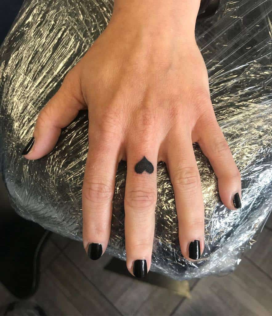 Small solid black heart tattoo, creating a bold yet subtle statement
