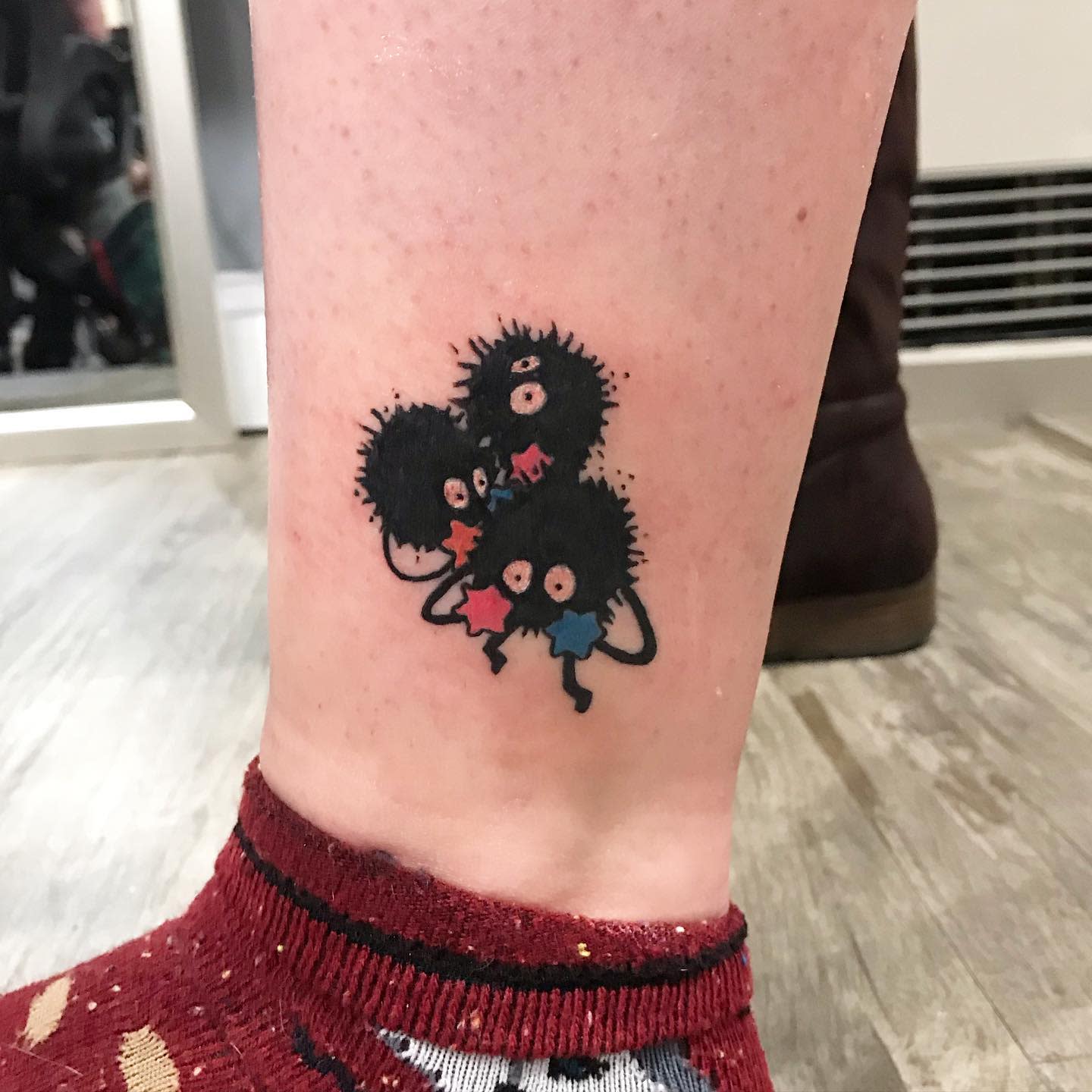 Tattoo of three black soot sprite characters holding stars on a leg above an ankle