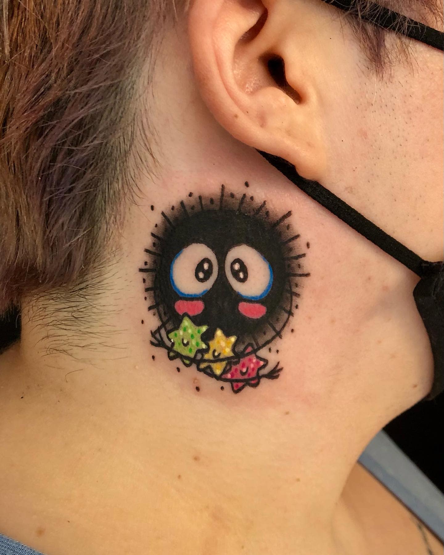 Tattoo of a soot sprite with star candies on the side of their neck