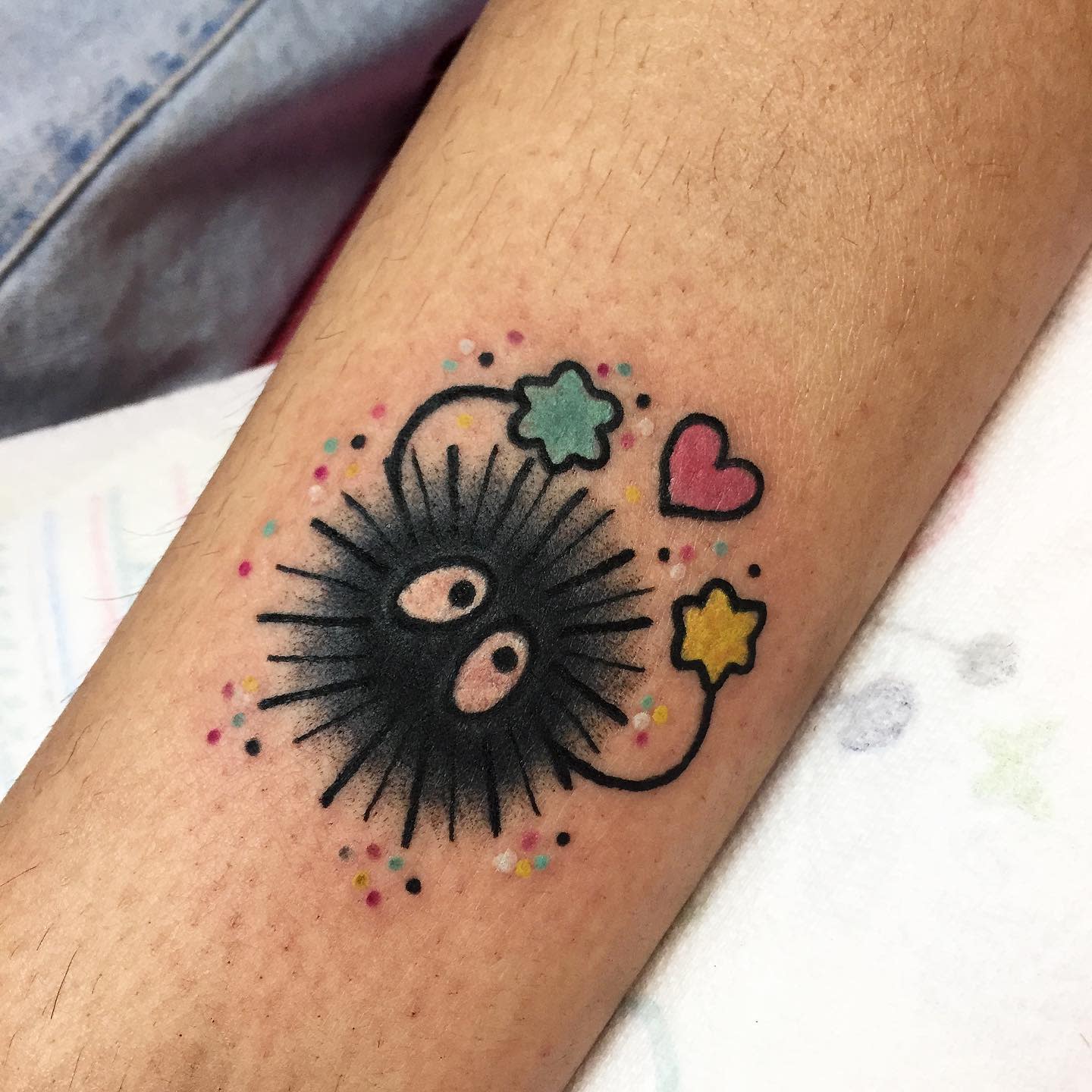 Tattoo featuring a black soot sprite holding a star and a heart, surrounded by colorful dots