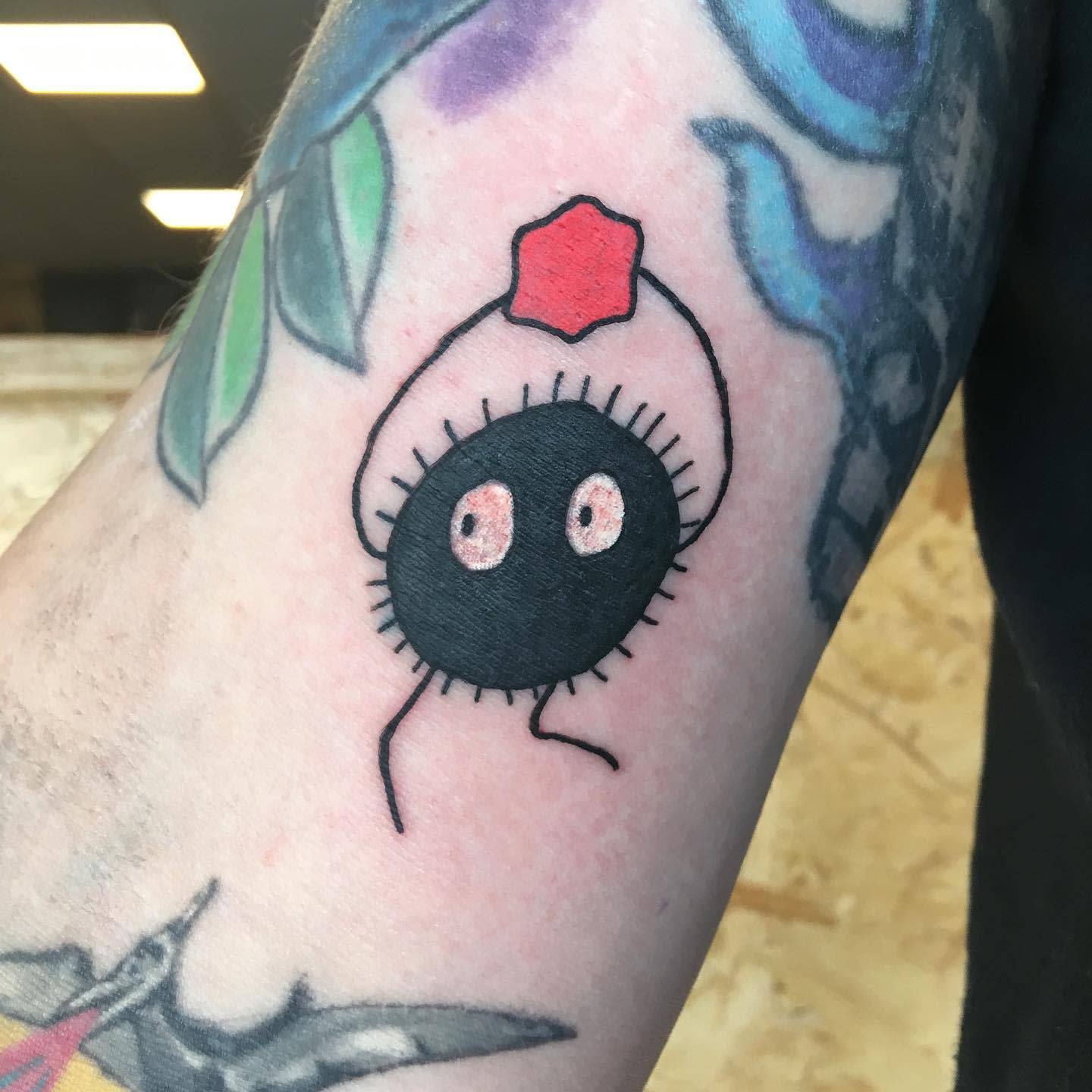 Tattoo of a soot sprite and a red hat on an arm