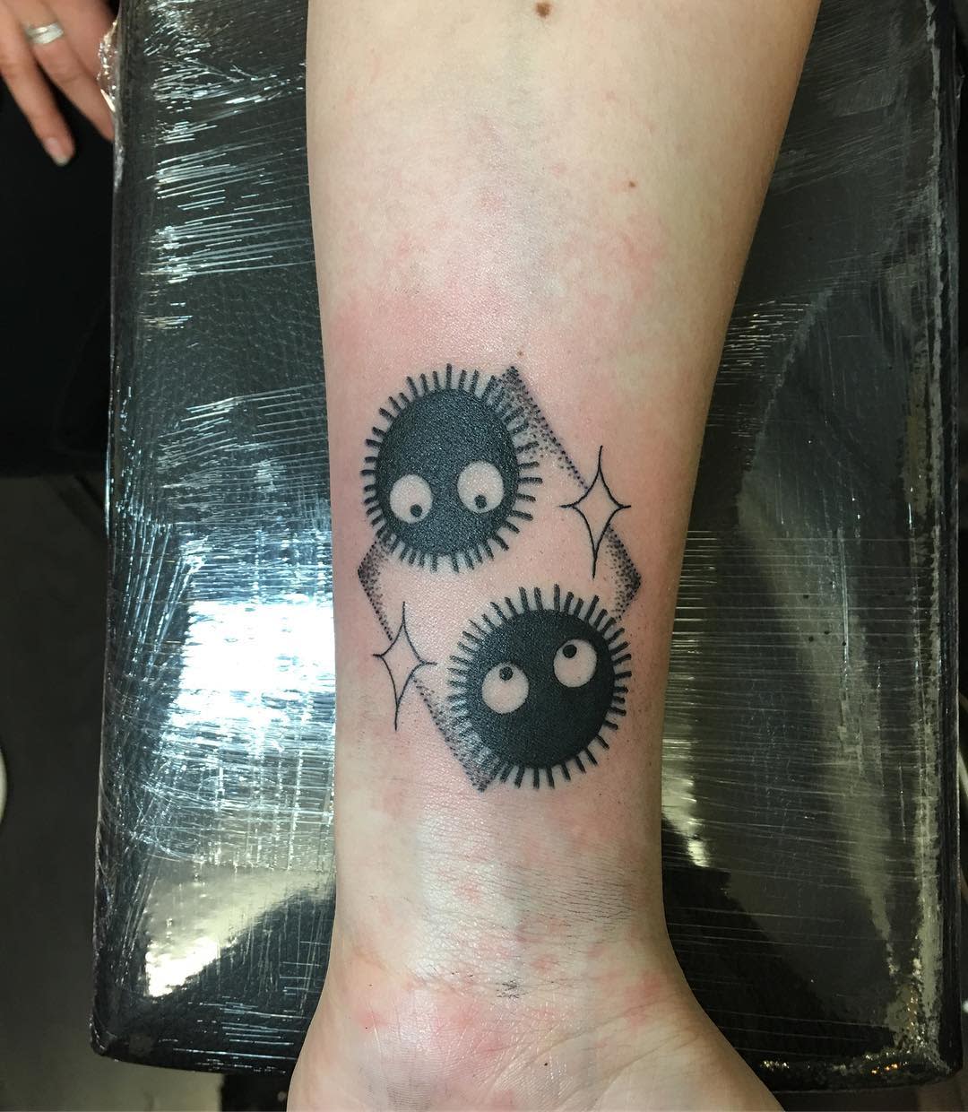 Tattoo of two soot sprites on an inner forearm with sparkling stars around them