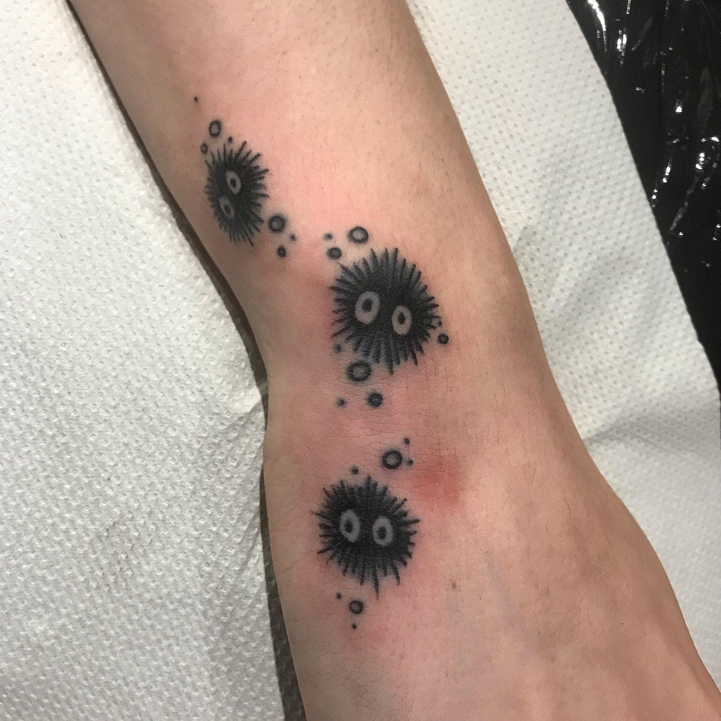 Tattoo of soot sprites with white eyes and small dots on the inner forearm