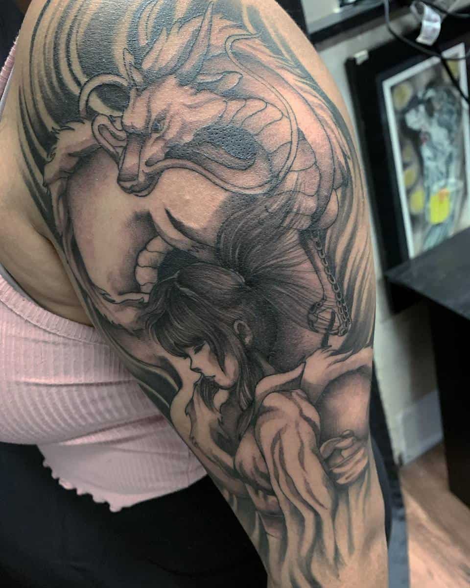Detailed black and gray tattoo of Chihiro embracing Haku in his dragon form from Spirited Away on the upper arm