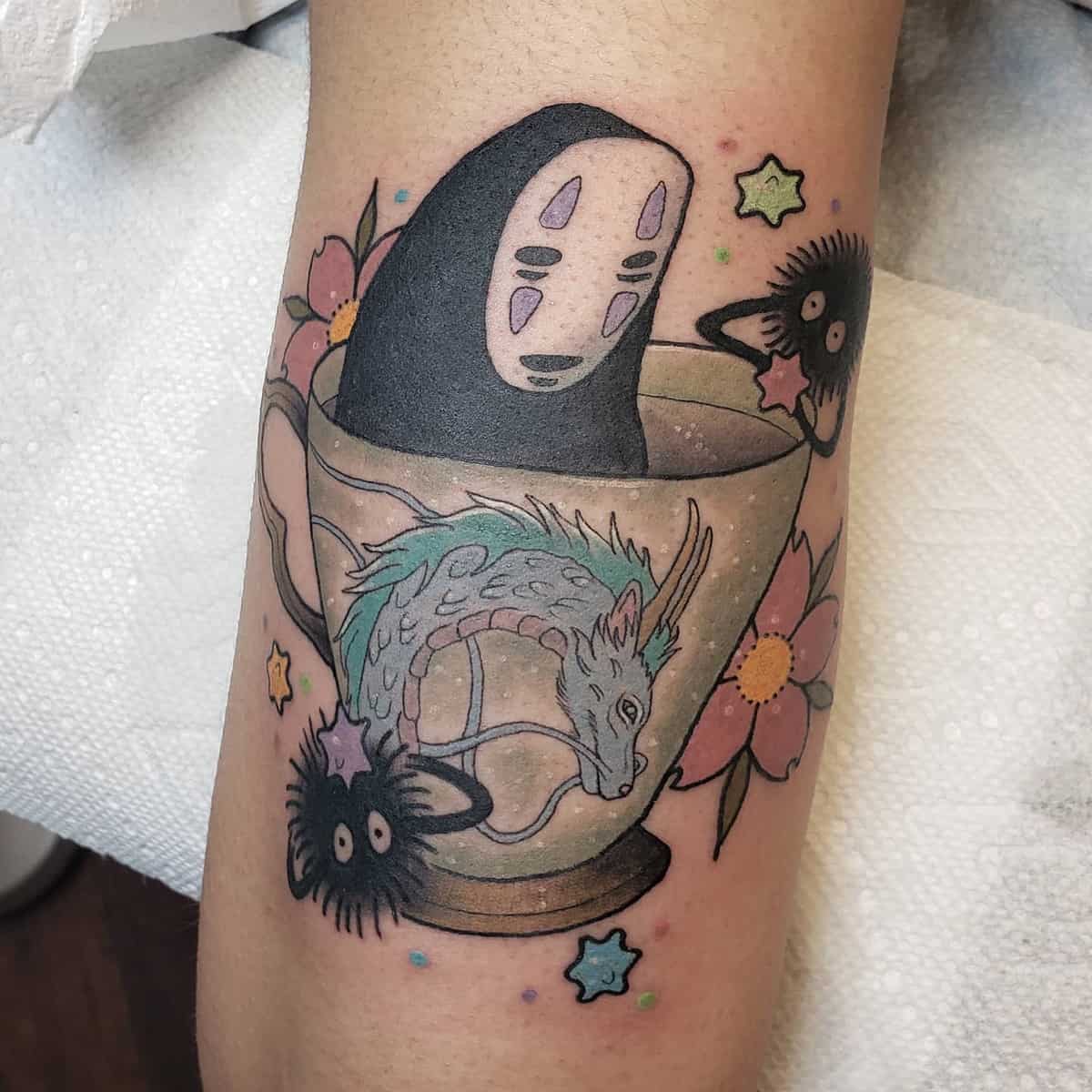 Colorful tattoo featuring No-Face, Haku, and soot sprites from Spirited Away in a teacup surrounded by flowers