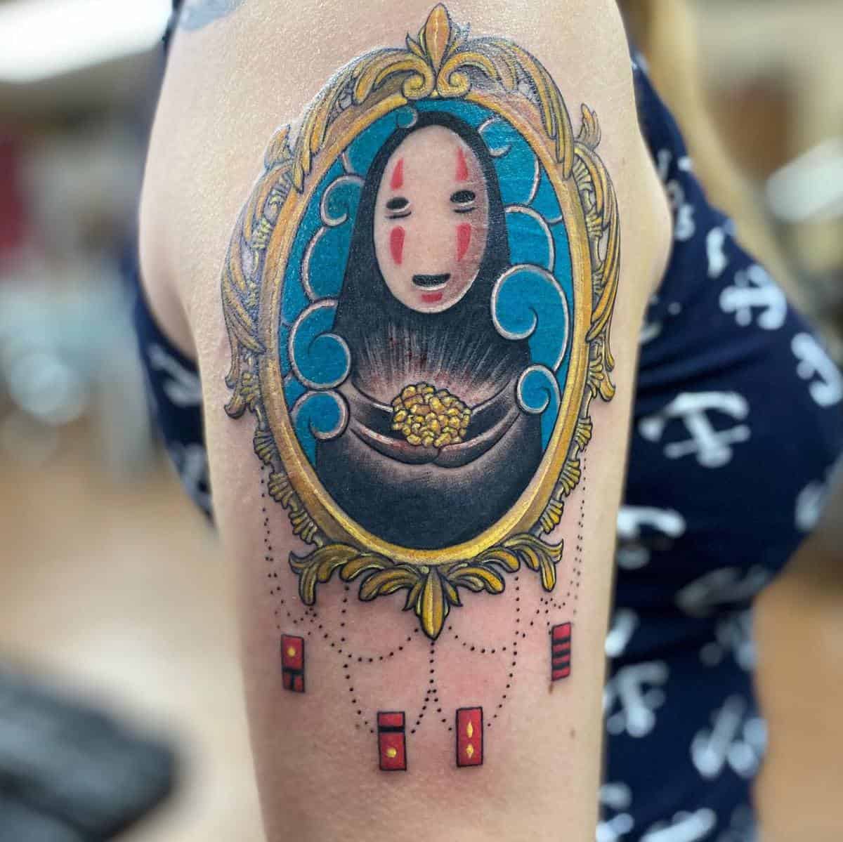 Colorful tattoo of No-Face from Spirited Away holding gold inside an ornate frame on the upper arm