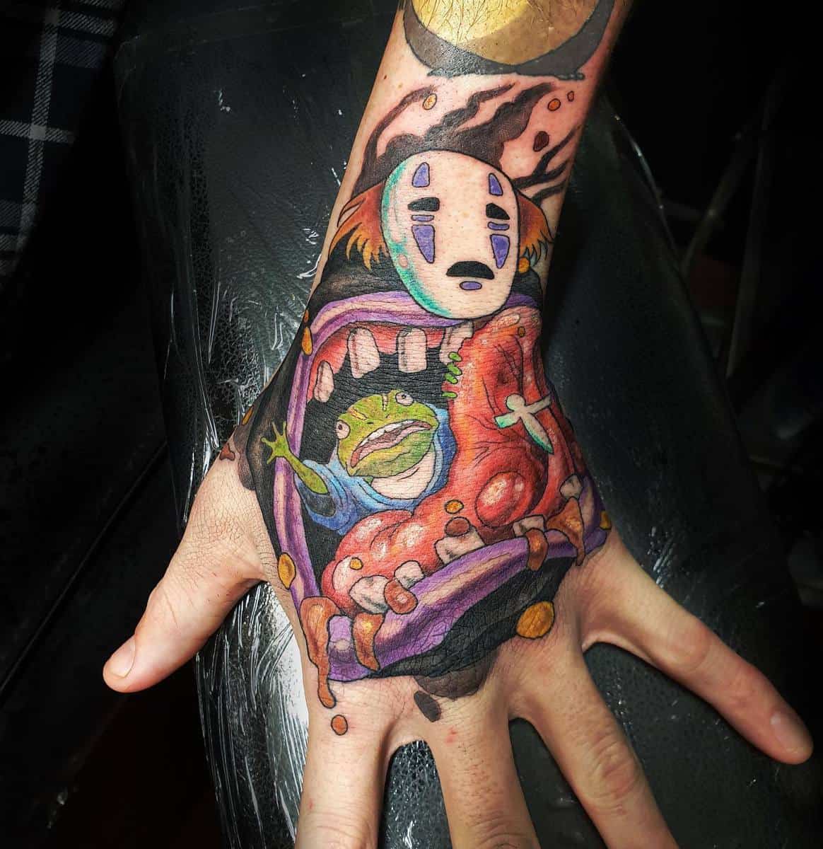 Vivid tattoo of No-Face from Spirited Away swallowing a frog on the back of the hand
